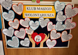 Tablica informacyjna Klubu Małego Wolontariusza ozdobiona kolorowymi serduszkami z opisami działań charytatywnych i projektów przedszkolnych.
