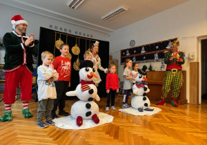Sześcioro dzieci wraz z elfami i panią Śnieżynką prezentują złożone przez dzieci bałwanki