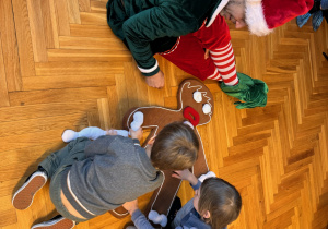 grupa chłlopców wraz z elfem dekourją dla Świętego Mikołaja duży pierniczek z materiału.