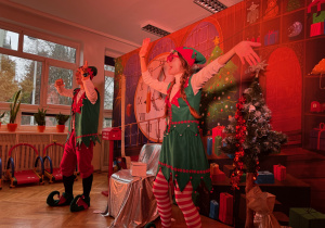 zdjęcie przedstawia scenę z teatrzyku Elfy i fabryka prezentów, kiedy elfy tańczą na tle świątecznych dekoracji