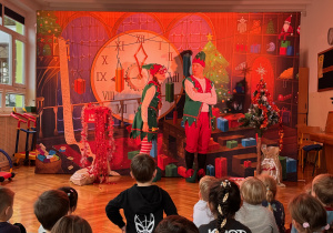 Przedszkolaki z zainteresowaniem oglądają przedstawienie teatralne „Elfy i fabryka prezentów”. Aktorzy w barwnych, świątecznych kostiumach przenoszą dzieci do magicznego świata elfów i fabryki prezentów