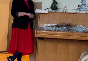 Pani Dyrektor Przedszkola nr 255 w czerwonej sukience i czarnym żakiecie podczas śpiewania kolędy "Oj Maluśki, Maluśki"