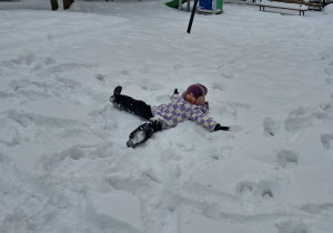 Dziewczynka z grupy czwartej robi aniołki na zaśnieżonym boisku przedszkolnym